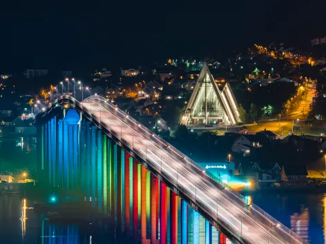 The Tromsø bridge lit up in colours, with the Arctic Cathedral in the background