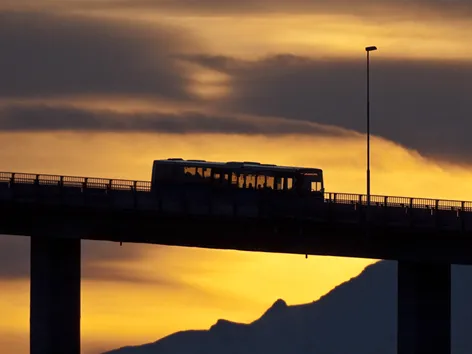 Bus driving over bridge with orange sky backdrop