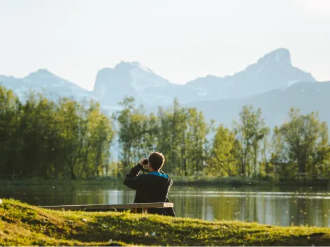 man looks through binoculars at the mountain from Prestvannet