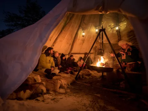 En gruppe mennesker sitter rundt et bål inni en lavvo