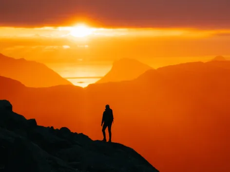 Siluett som ser på solnedgangen fra en fjelltopp på Kvaløya