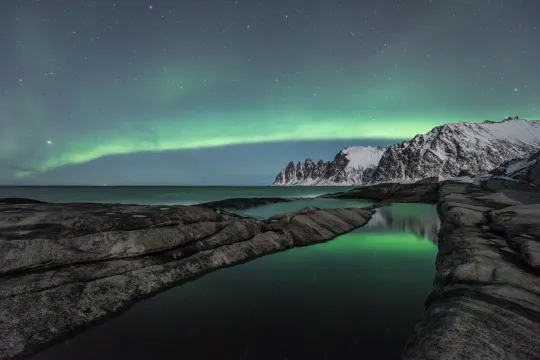 Northern lights above sea and mountains