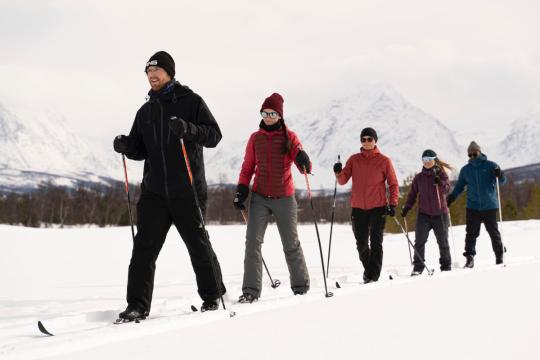 fem personer som går på ski med Lyngsalpene i bakgrunnen