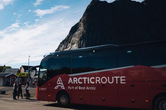 The Arctic Route red bus with mountains in the background.