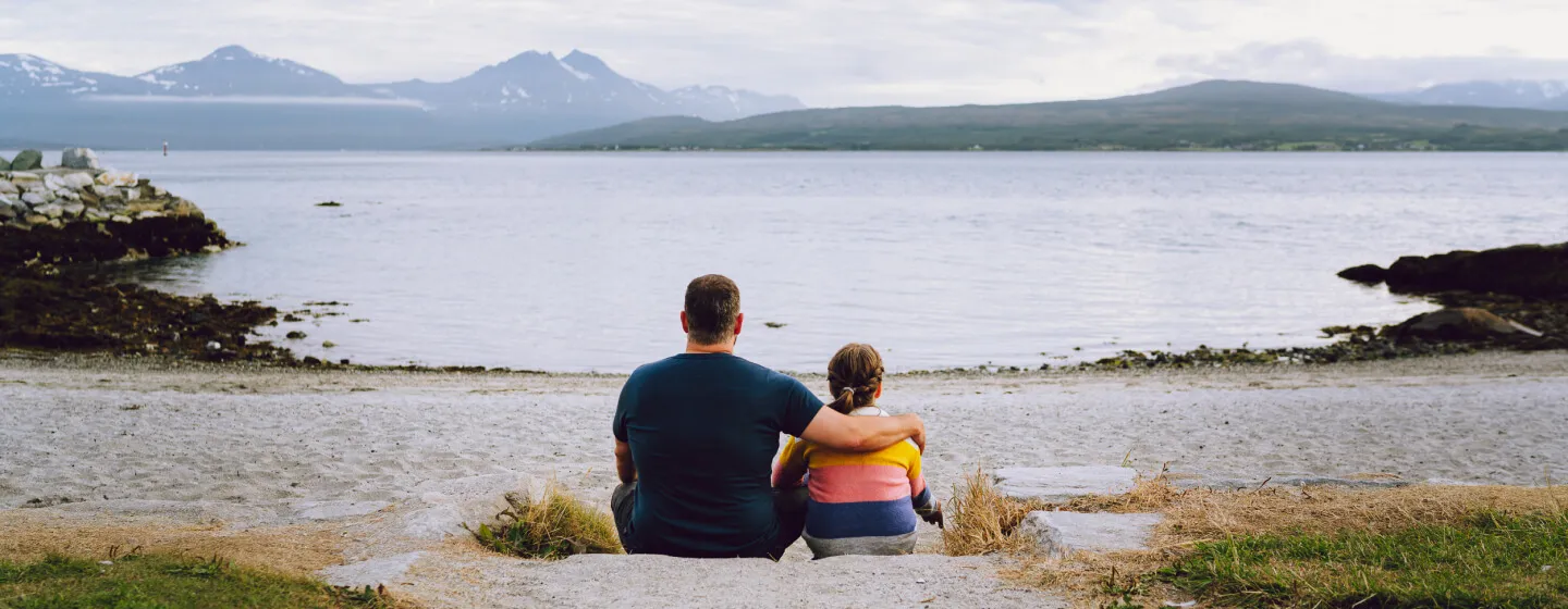 Far og datter sitter ved stranda i Telegrafbukta i Tromsø og ser utover havet