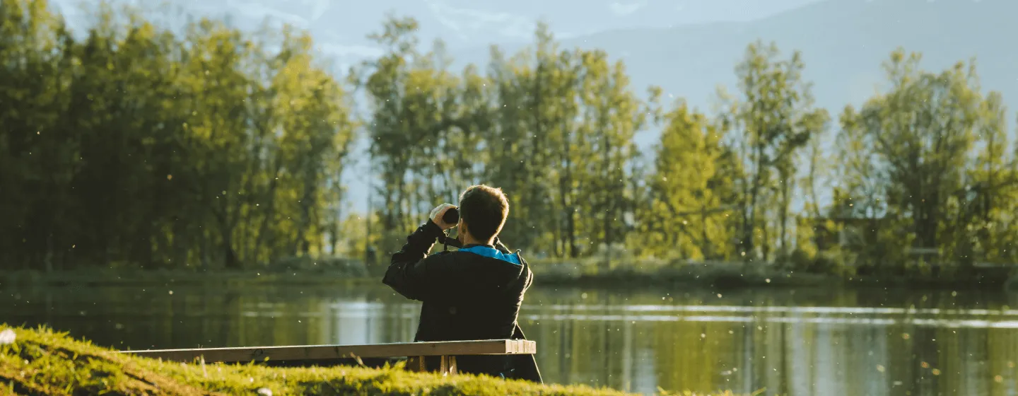 man looks through binoculars at the mountain from Prestvannet