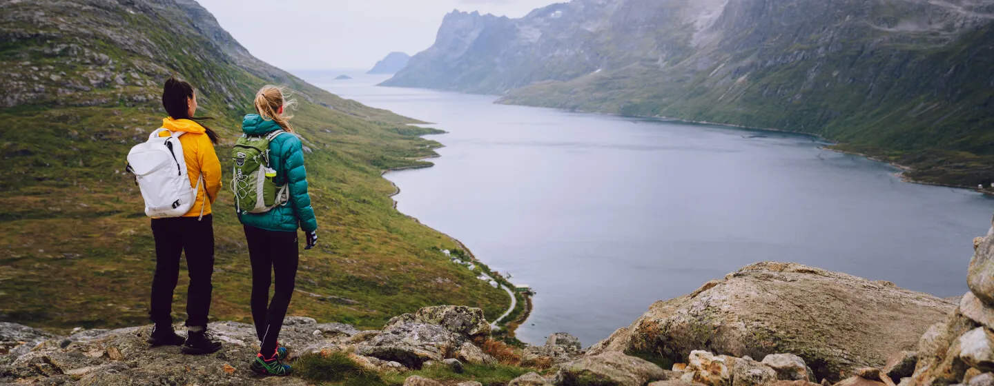 Two people standing on a mountain looking a the landscape.