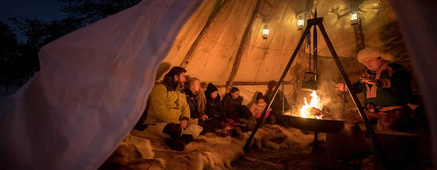 En gruppe mennesker sitter rundt et bål inni en lavvo