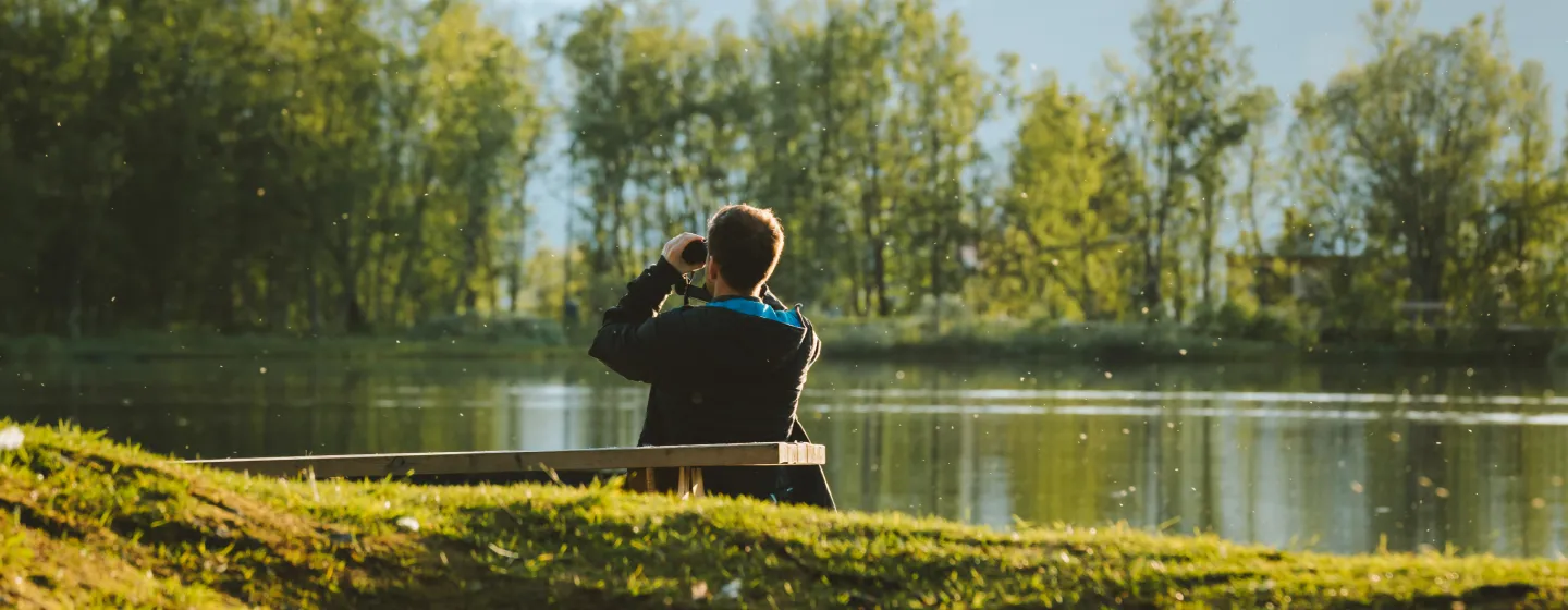 Person sitting on a bench looking at the mountains with binoculars.