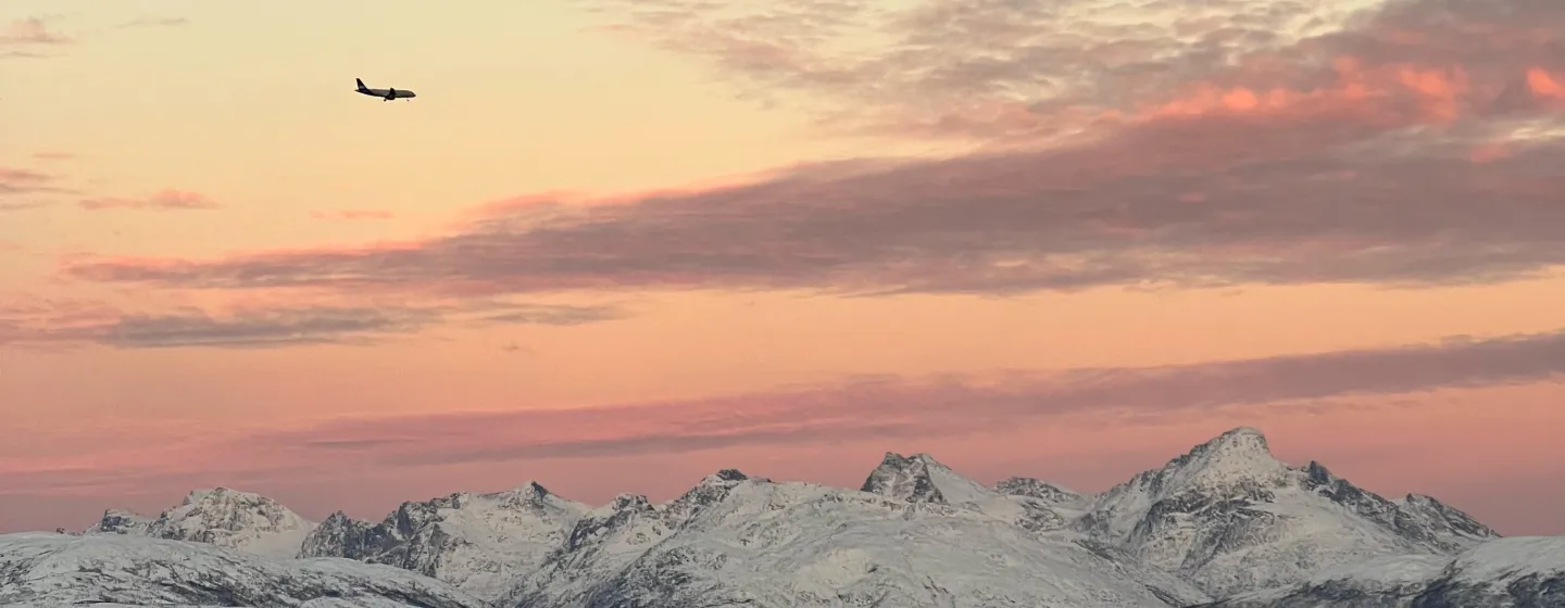 Et fly flyr over snøkledde fjell.