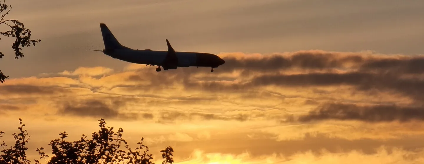 An airplane in the sky with sunset in the background.